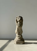 Stone lion statue on a white pedestal against a plain wall.