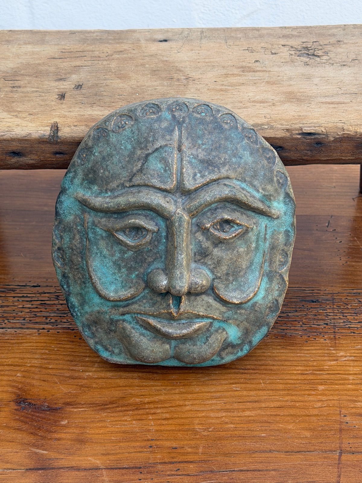 Close-up of face wall plaque with raised features and verdigris finish