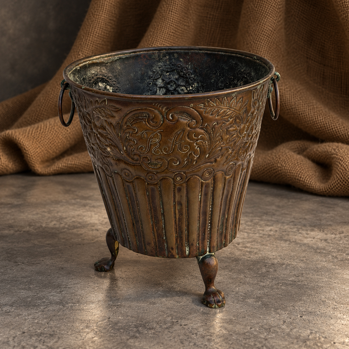 Side profile of the brass cachepot showing floral detailing and the shape of its supporting feet.