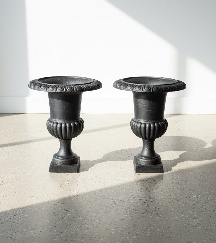 Pair of 29" French Cast Iron Urn Black Planters on a polished concrete floor, showcasing antique finish and elegant design. hommes + gardens estudio.